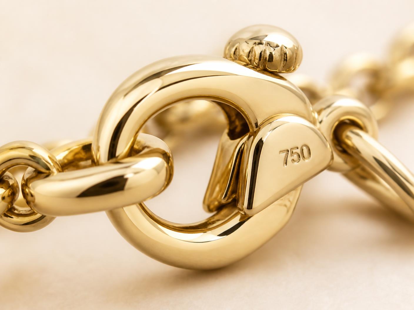 Extreme close-up of a polished gold necklace clasp stamped 750, shown on an ivory background