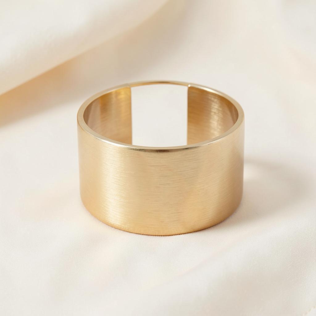 Gara wide cuff bracelet in brushed gold standing upright on ivory silk